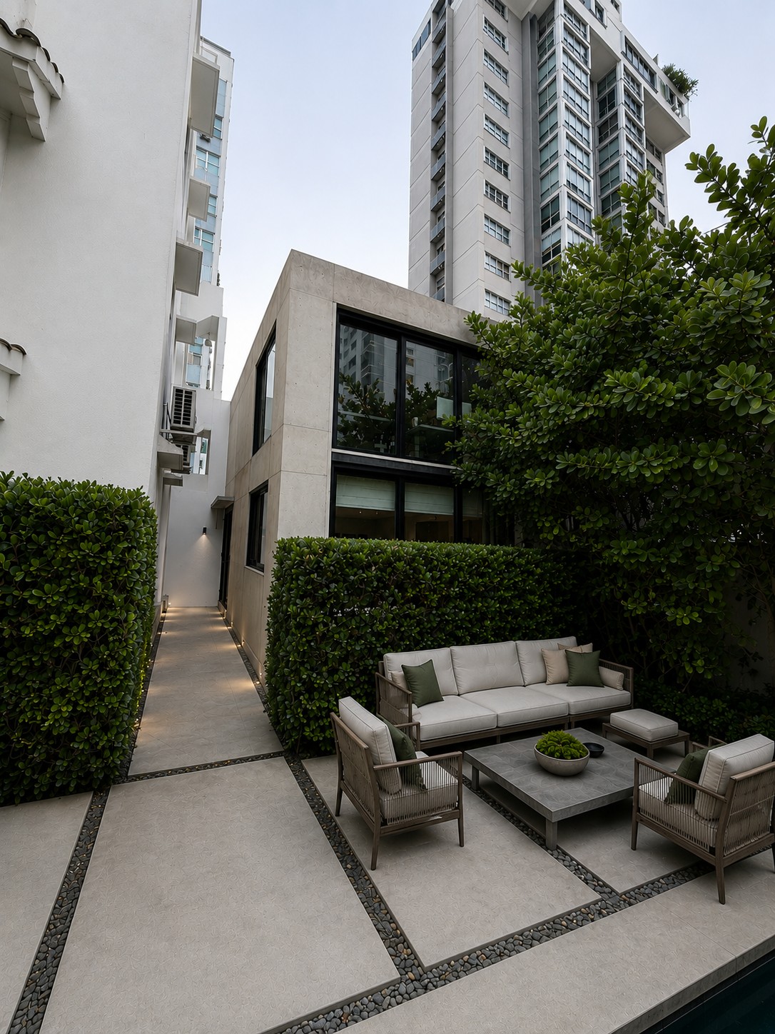 Garden terrace at dusk — clipped hedges, lounge seating and the lit side path